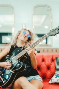 happy young female guitarist having fun on couch at home