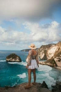 unrecognizable stylish female tourist contemplating wavy sea from rock