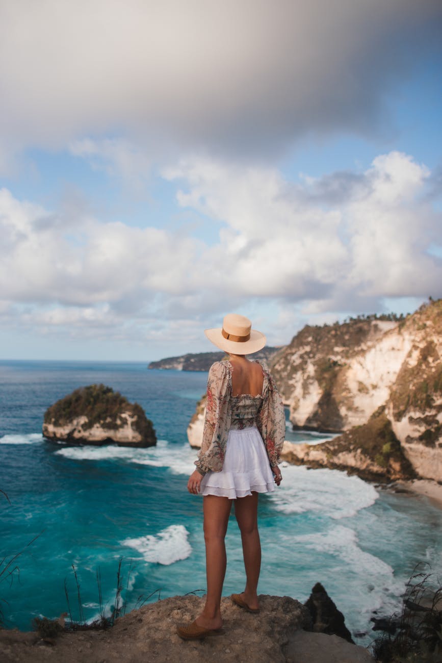 unrecognizable stylish female tourist contemplating wavy sea from rock
