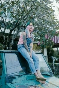 young woman with pink hair sitting on aged car roof