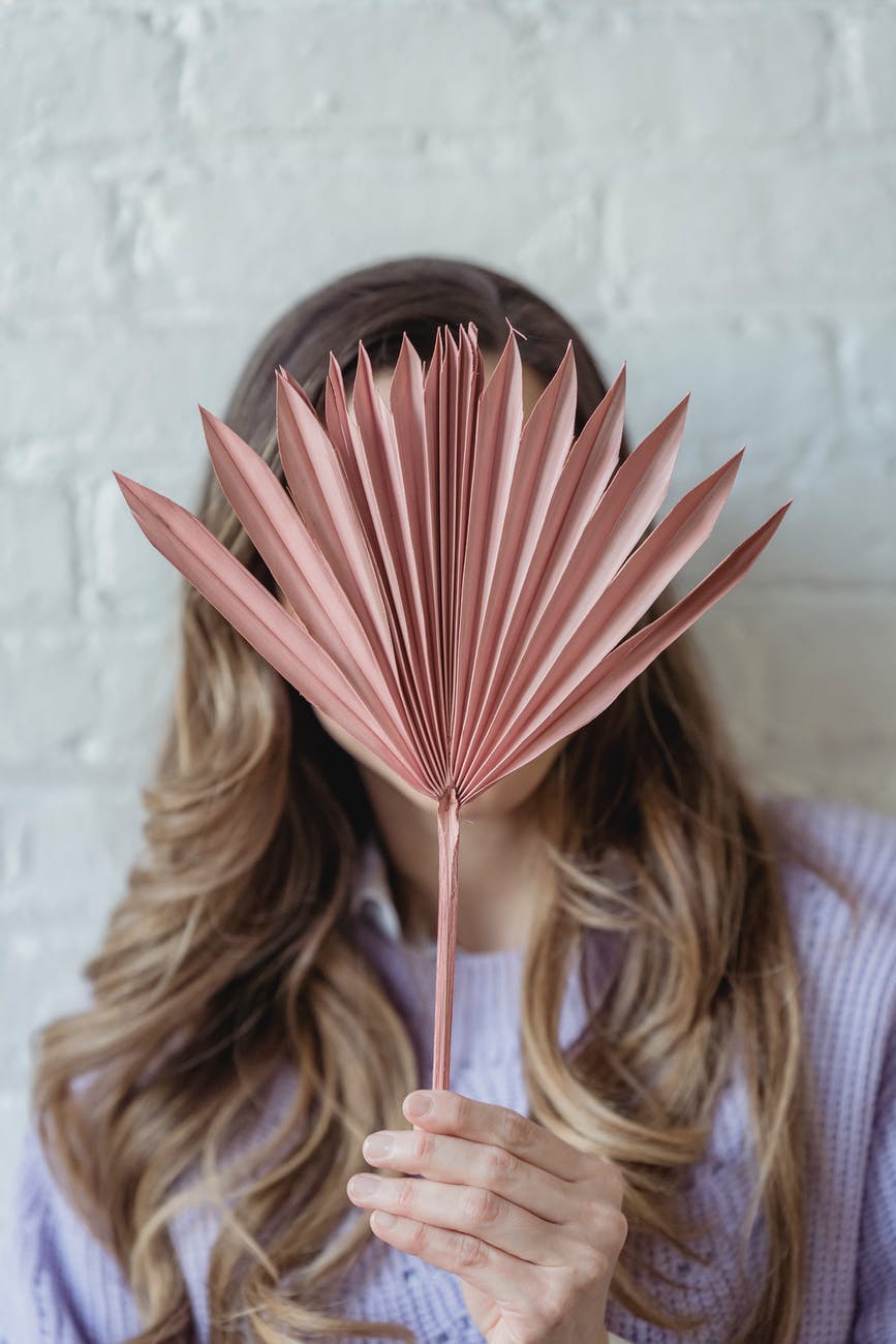 woman covering face behind branch of plant